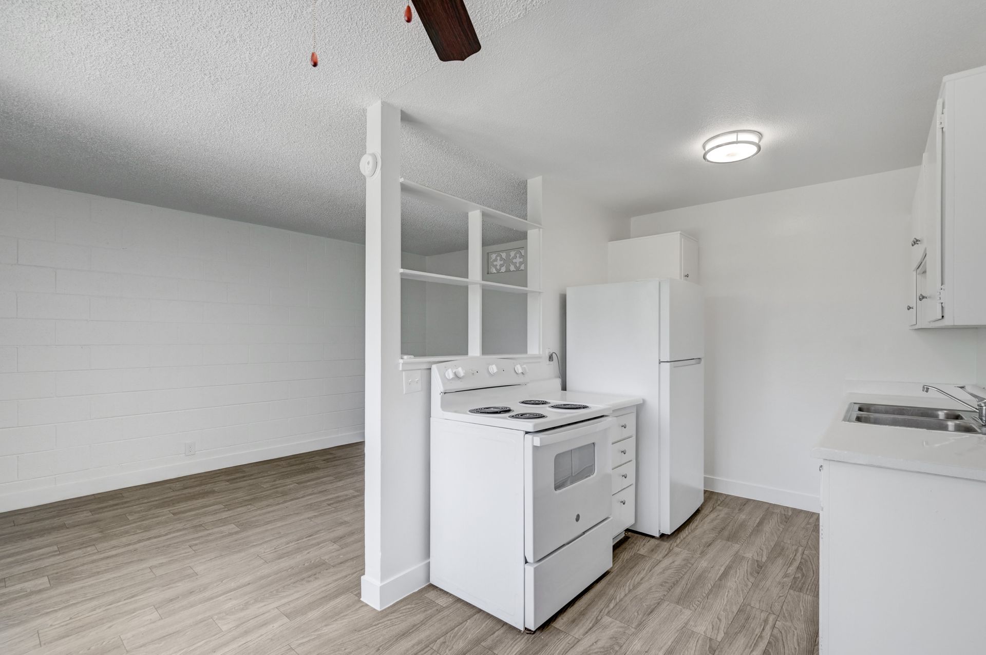 Empty kitchen and living area with white appliances, light wood flooring, and white walls