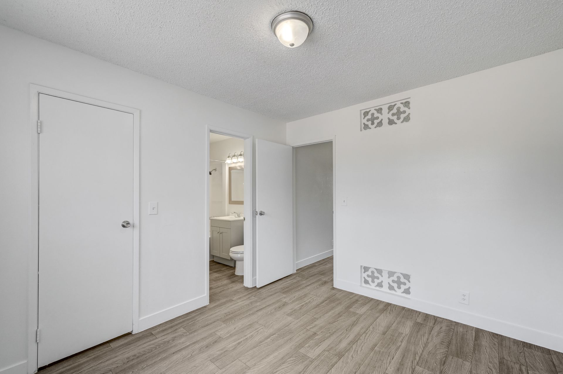 Empty white bedroom with wood floors, open closet, and doorway to a bathroom