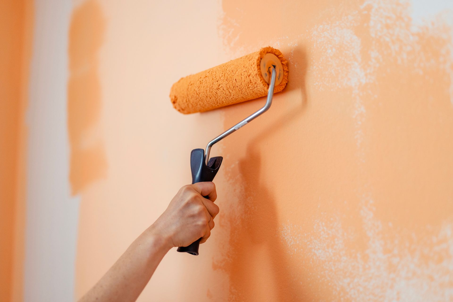 A person is painting a wall with an orange paint roller