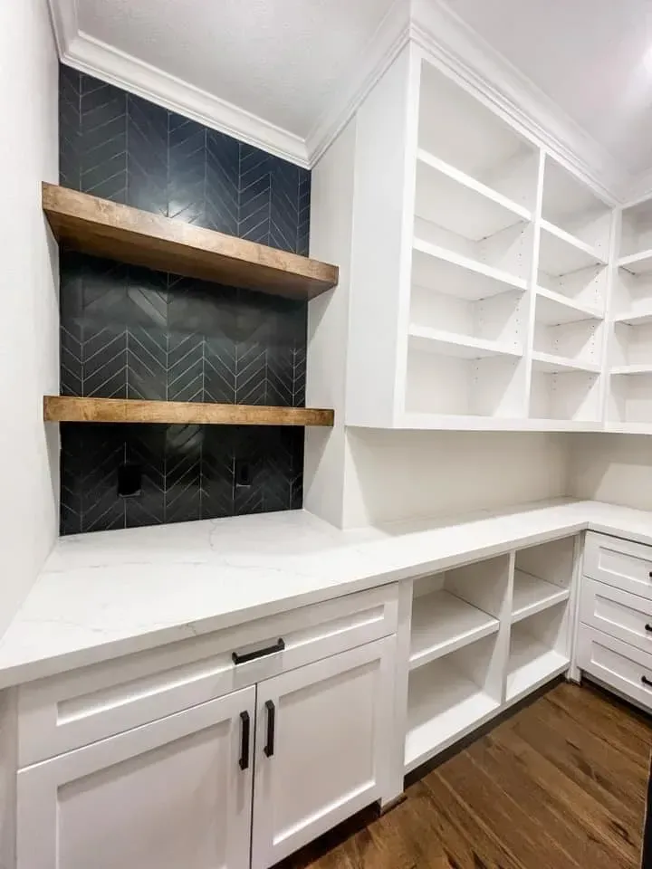 A kitchen with white cabinets and shelves and a wooden floor.