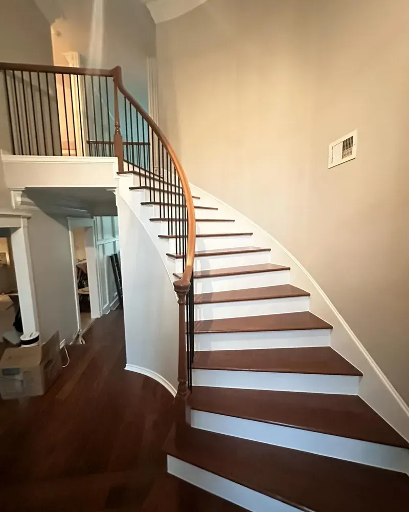 A curved staircase with white steps and a wooden railing in a house.