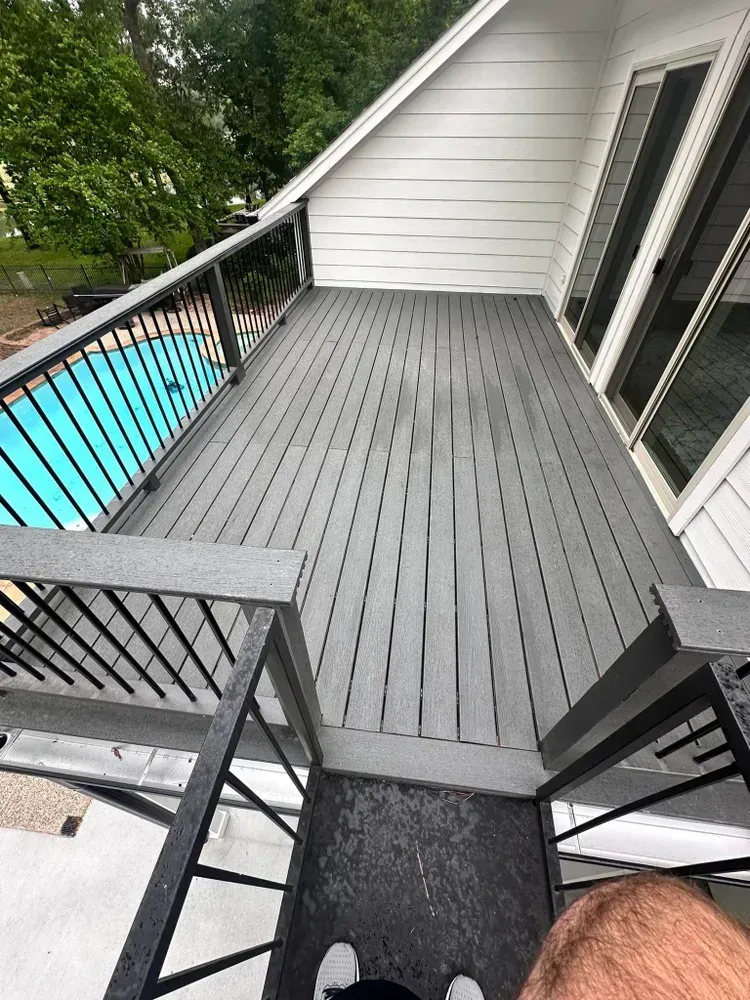 A man is standing on a balcony overlooking a pool.