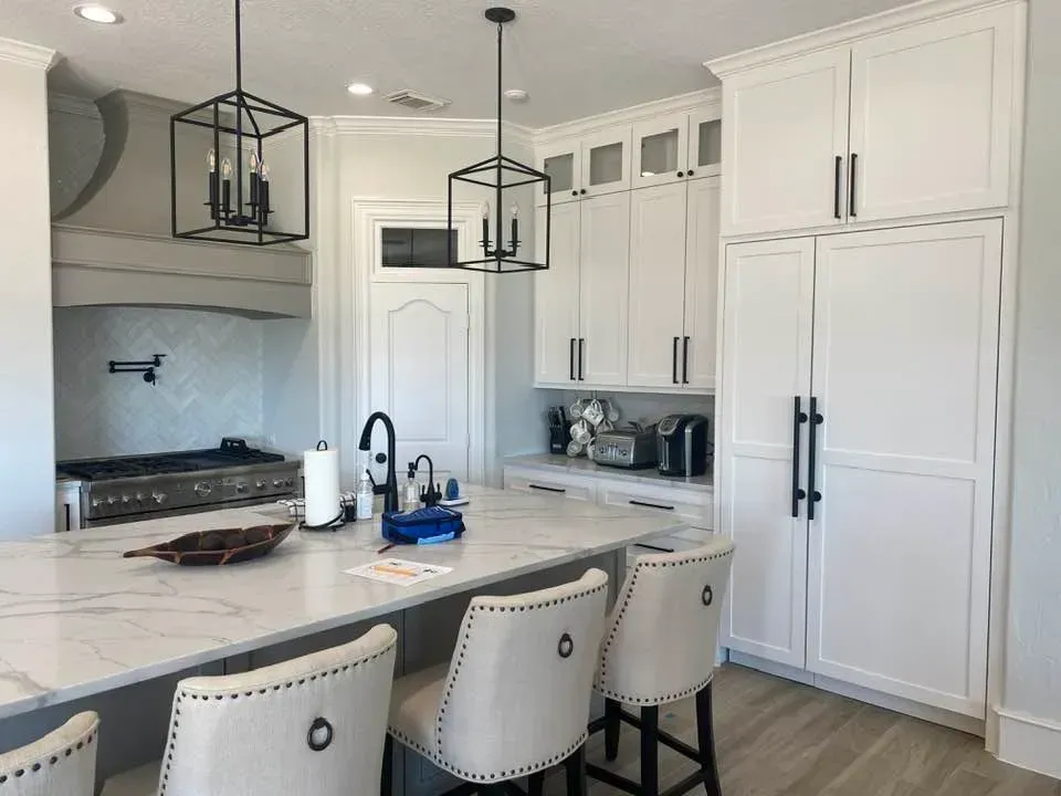 A kitchen with white cabinets , a large island , a stove and a refrigerator.