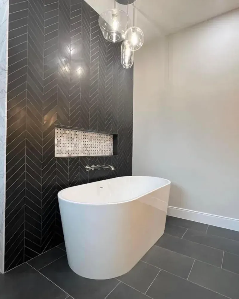 There is a bathtub in the bathroom with black tiles.