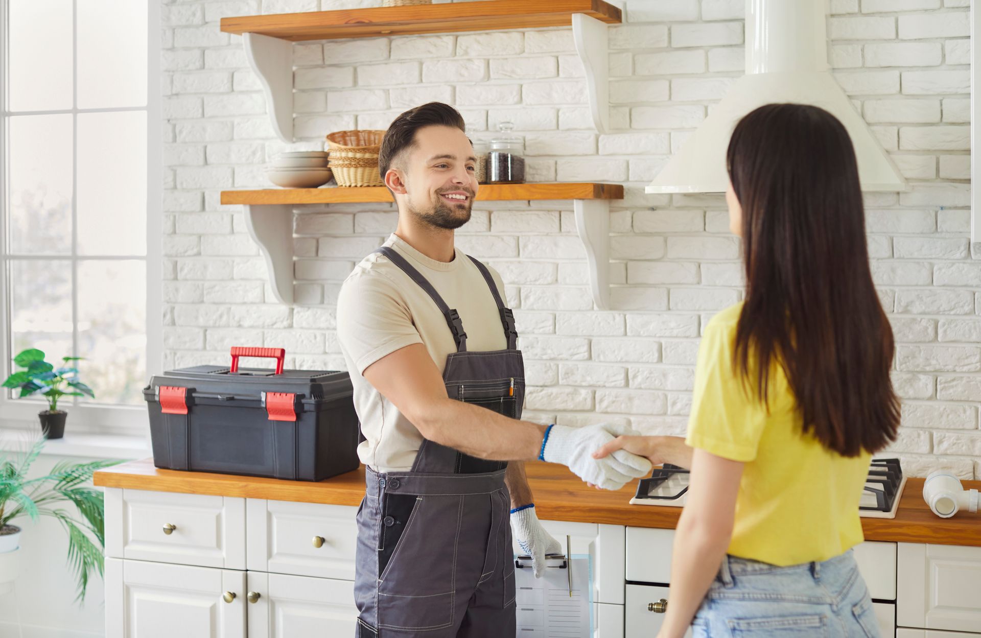 Worker shaking hands with a person in a kitchen next to a toolbox.