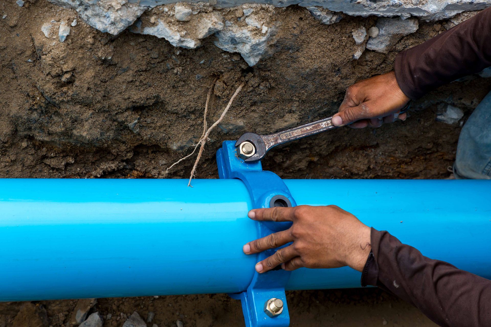 Technician repairing underground pipe with wrench during water line services installation work.