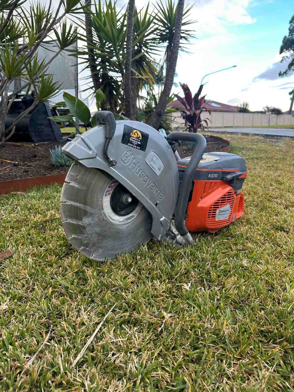 A Concrete Saw is Sitting on Top of a Lush Green Field — Garrett's Excavation & Equipment Hire in Sanctuary Point, NSW