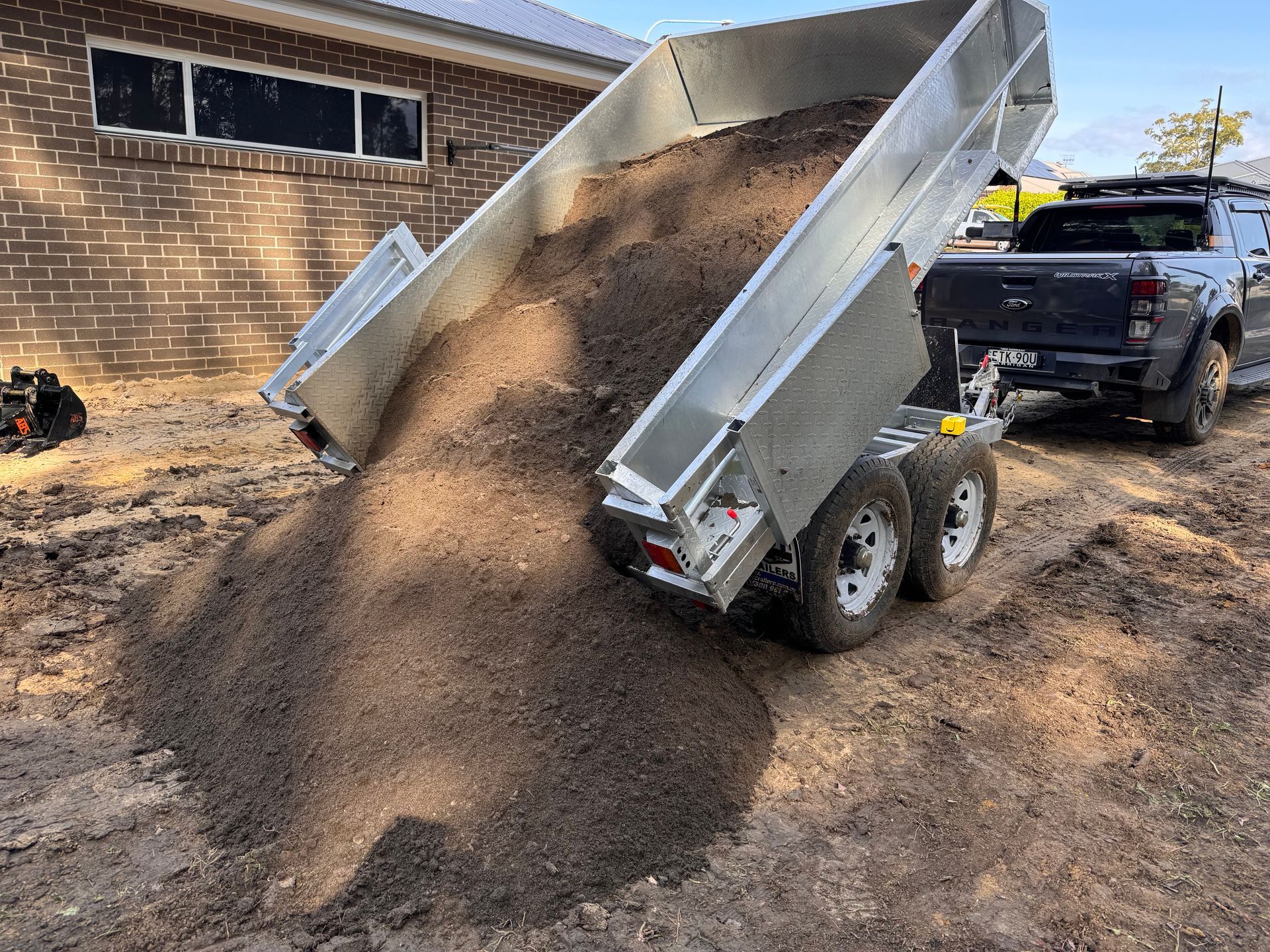 A Dump Truck is Loading Dirt Into a Trailer — Garrett's Excavation & Equipment Hire in Sanctuary Point, NSW