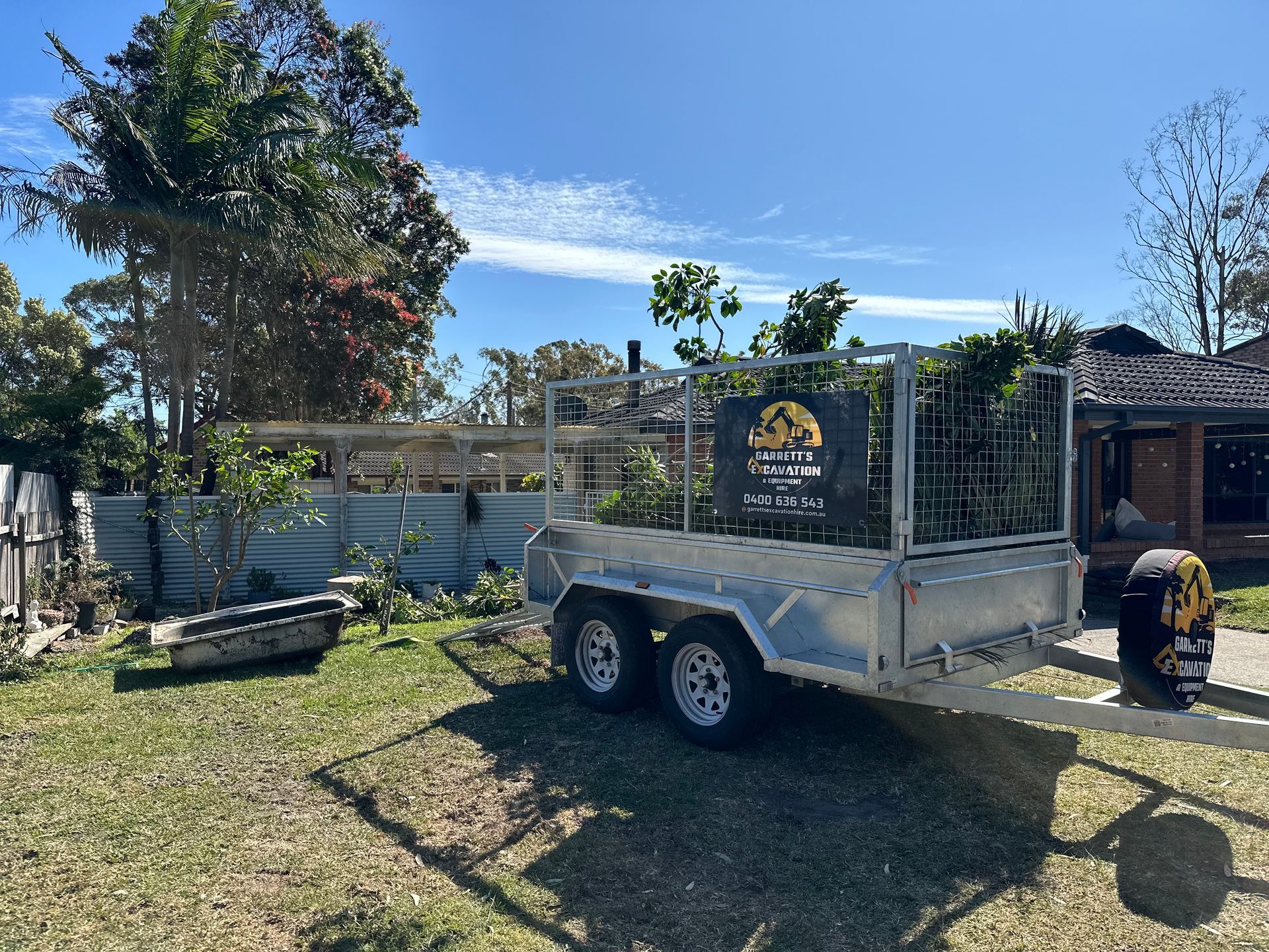A Trailer is Parked in a Grassy Yard in Front of a House — Garrett's Excavation & Equipment Hire in Sanctuary Point, NSW