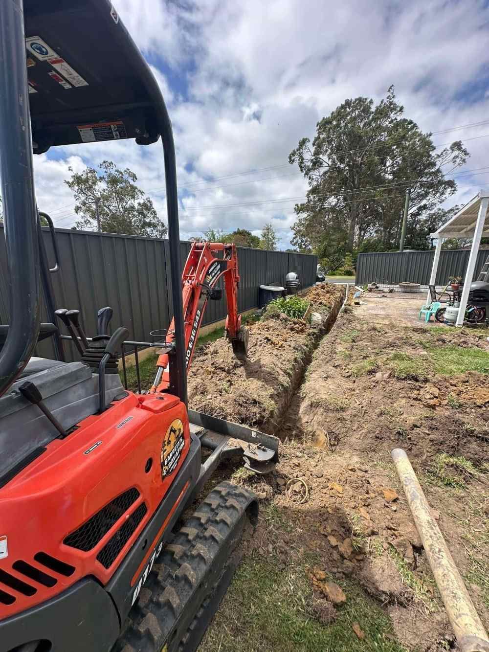 A Small Red Excavator is Digging a Trench in the Dirt — Garrett's Excavation & Equipment Hire in Sanctuary Point, NSW