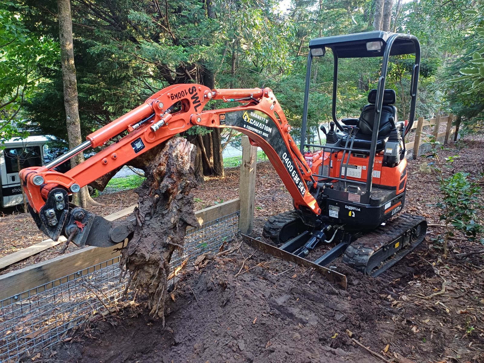 A Small Orange Excavator is Digging a Hole in the Ground — Garrett's Excavation & Equipment Hire in Sanctuary Point, NSW