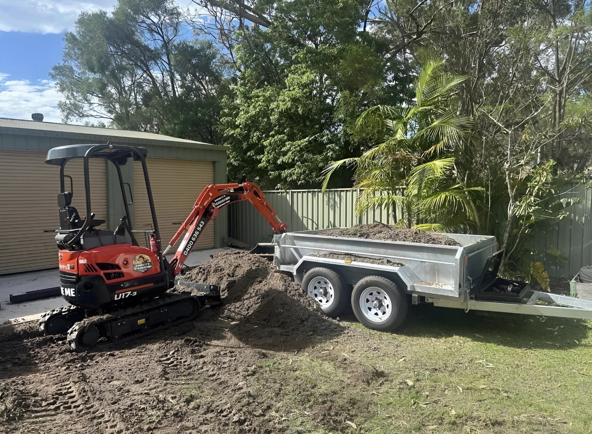 A Small Excavator is Parked Next to a Trailer in a Yard — Garrett's Excavation & Equipment Hire in Sanctuary Point, NSW