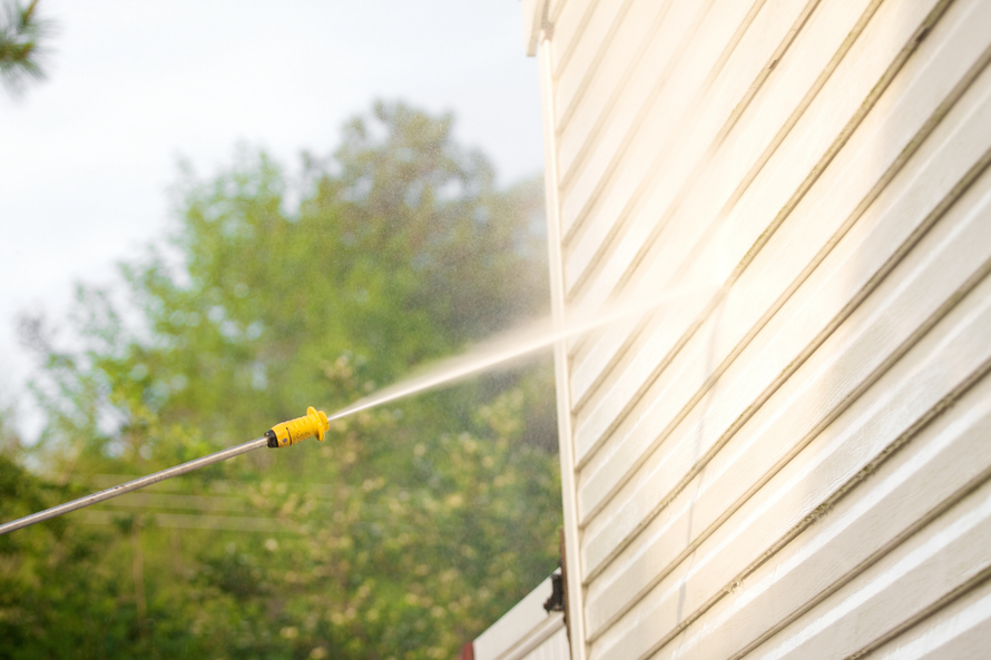 Pressure washing a house's beige siding with a spray nozzle outdoors