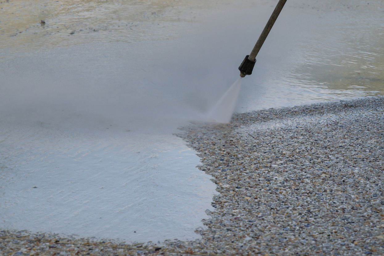 Pressure washer cleaning a concrete surface beside a pebble area under running water
