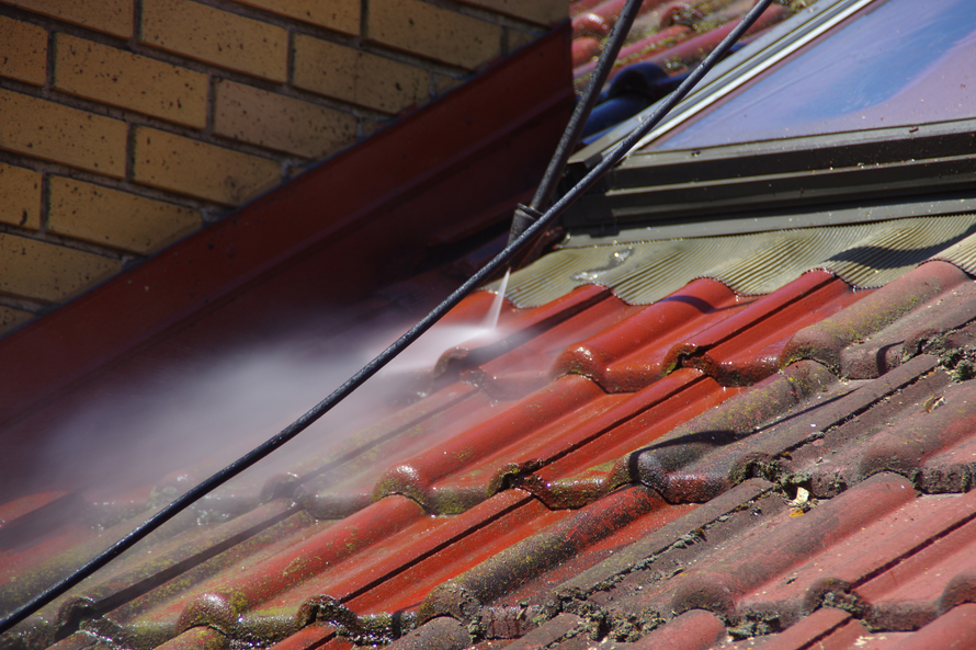 Water spraying from a hose onto a red tiled roof beside a brick wall