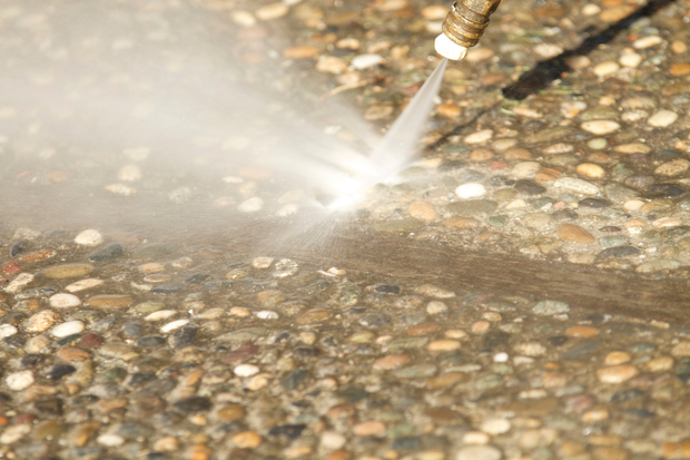 Person pressure washing a wet wooden deck with a spray nozzle in a fenced backyard.