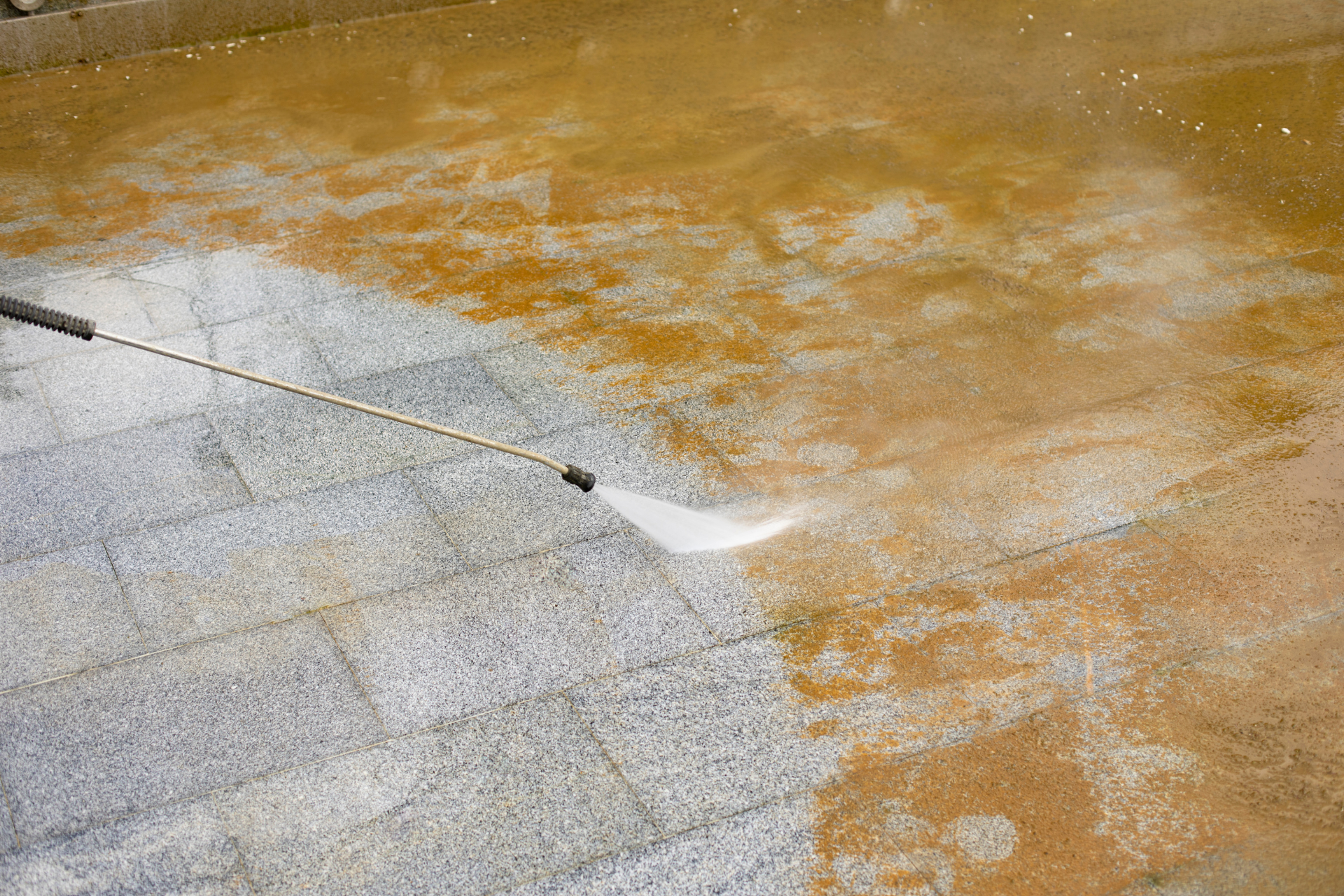 Concrete floor being pressure washed, with dirty water and a spray nozzle on a long pole