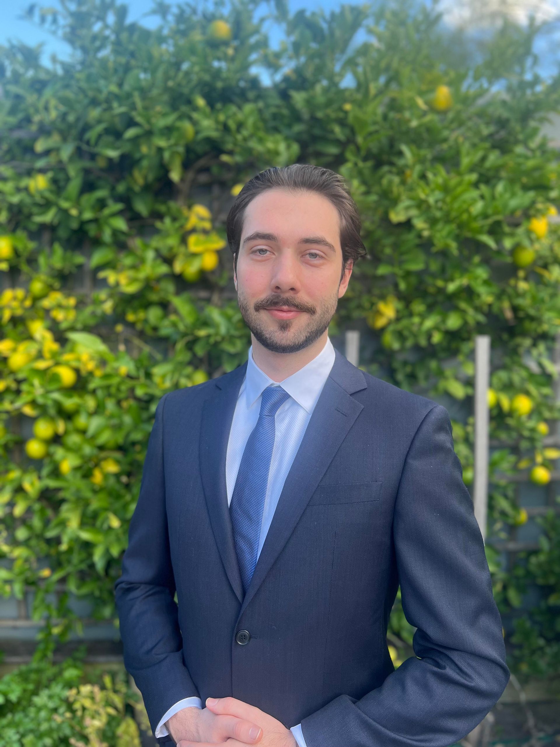 A man in a suit and tie is standing in front of a lemon tree.
