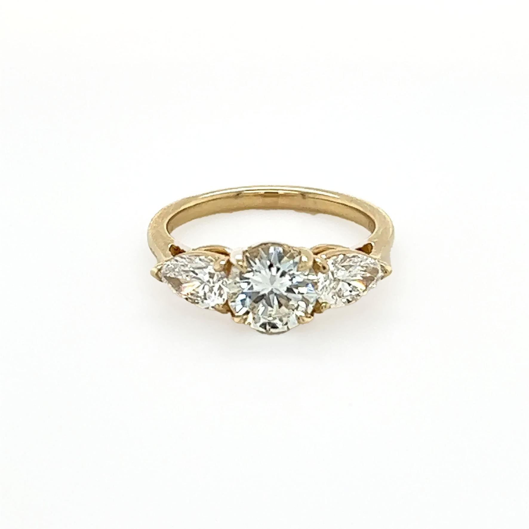 A yellow gold ring with three diamonds on a white surface.