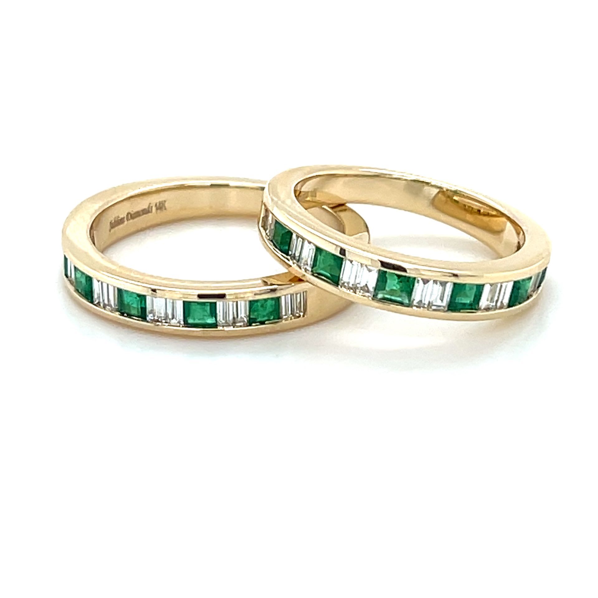 A pair of wedding rings with emeralds and diamonds on a white background.