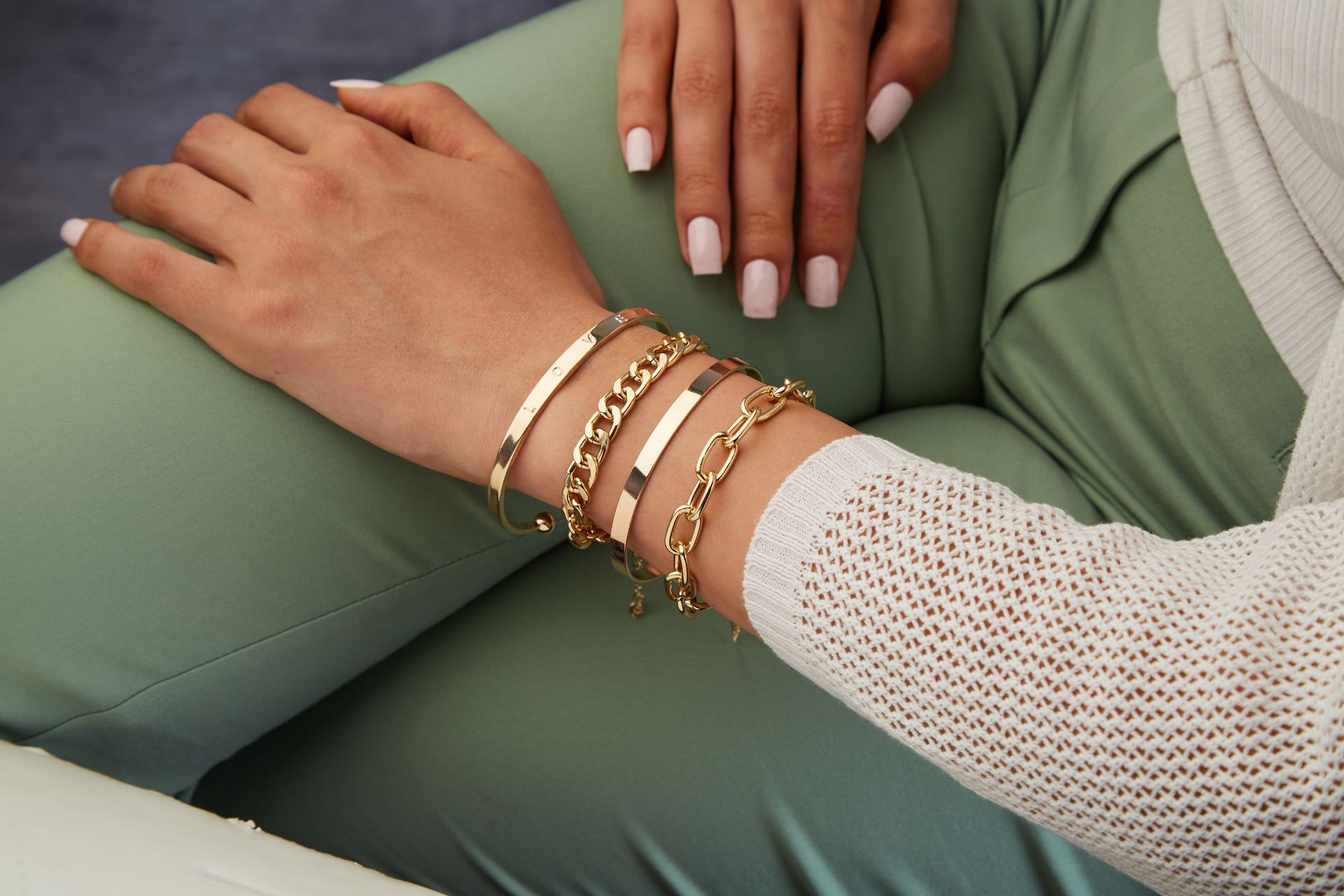 A woman wearing a white sweater and gold bracelets on her wrist.