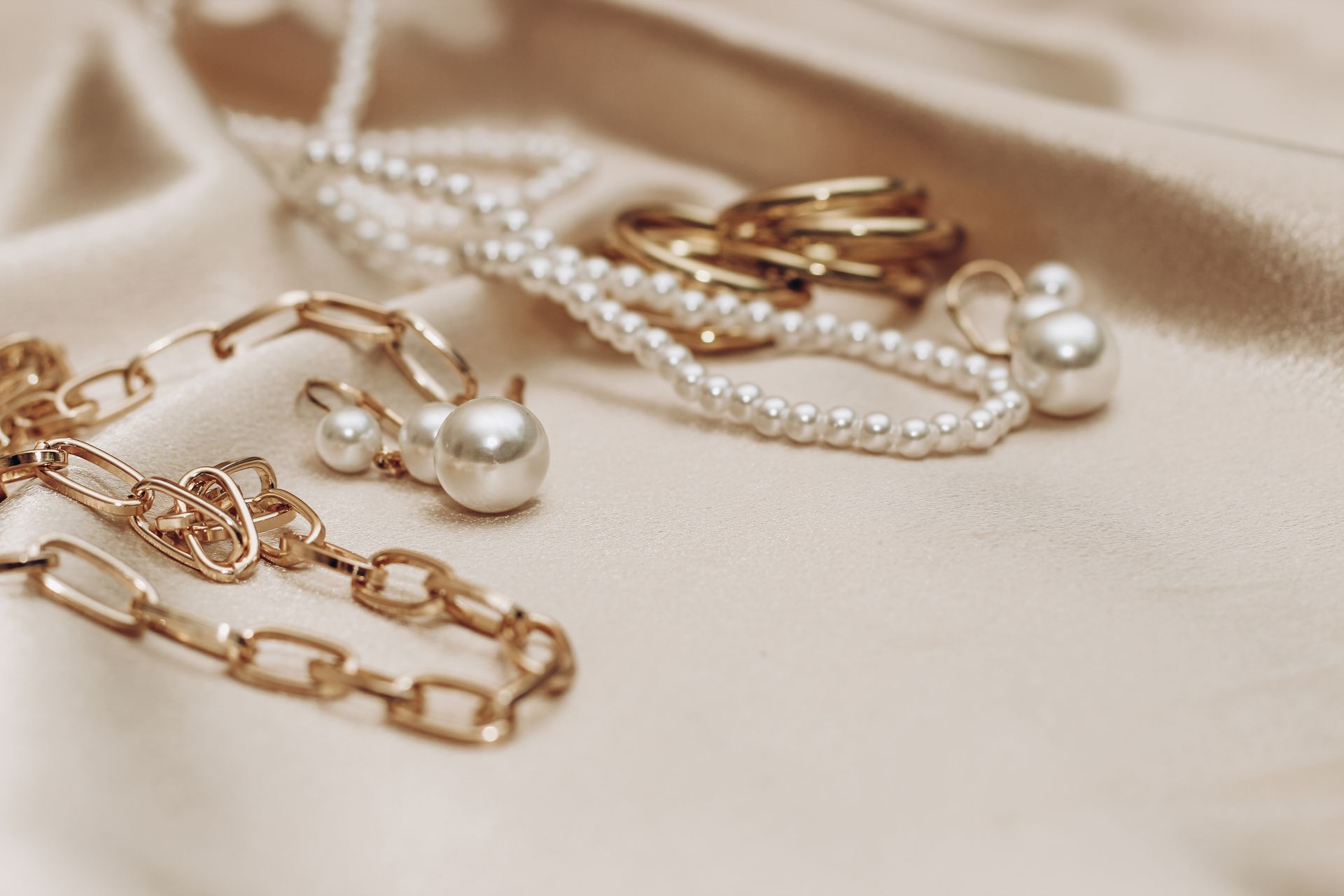 A close up of a necklace , earrings , rings and pearls on a cloth.