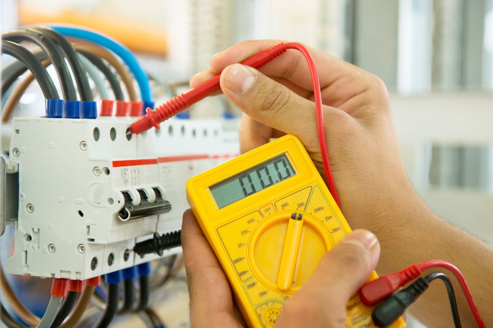 Person using a yellow multimeter to test electrical wiring in a breaker box.