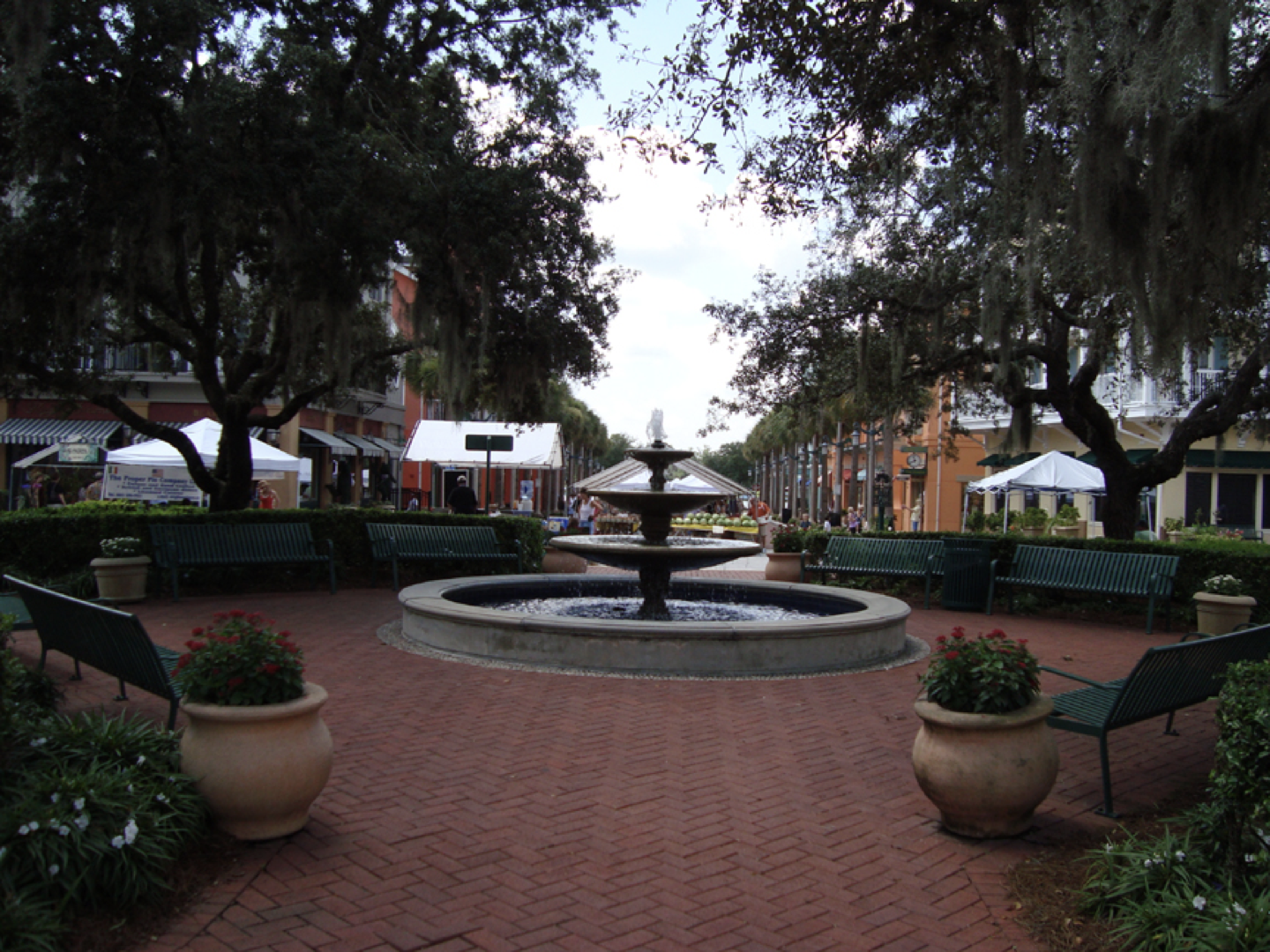 a fountain in a park with benches and potted plants