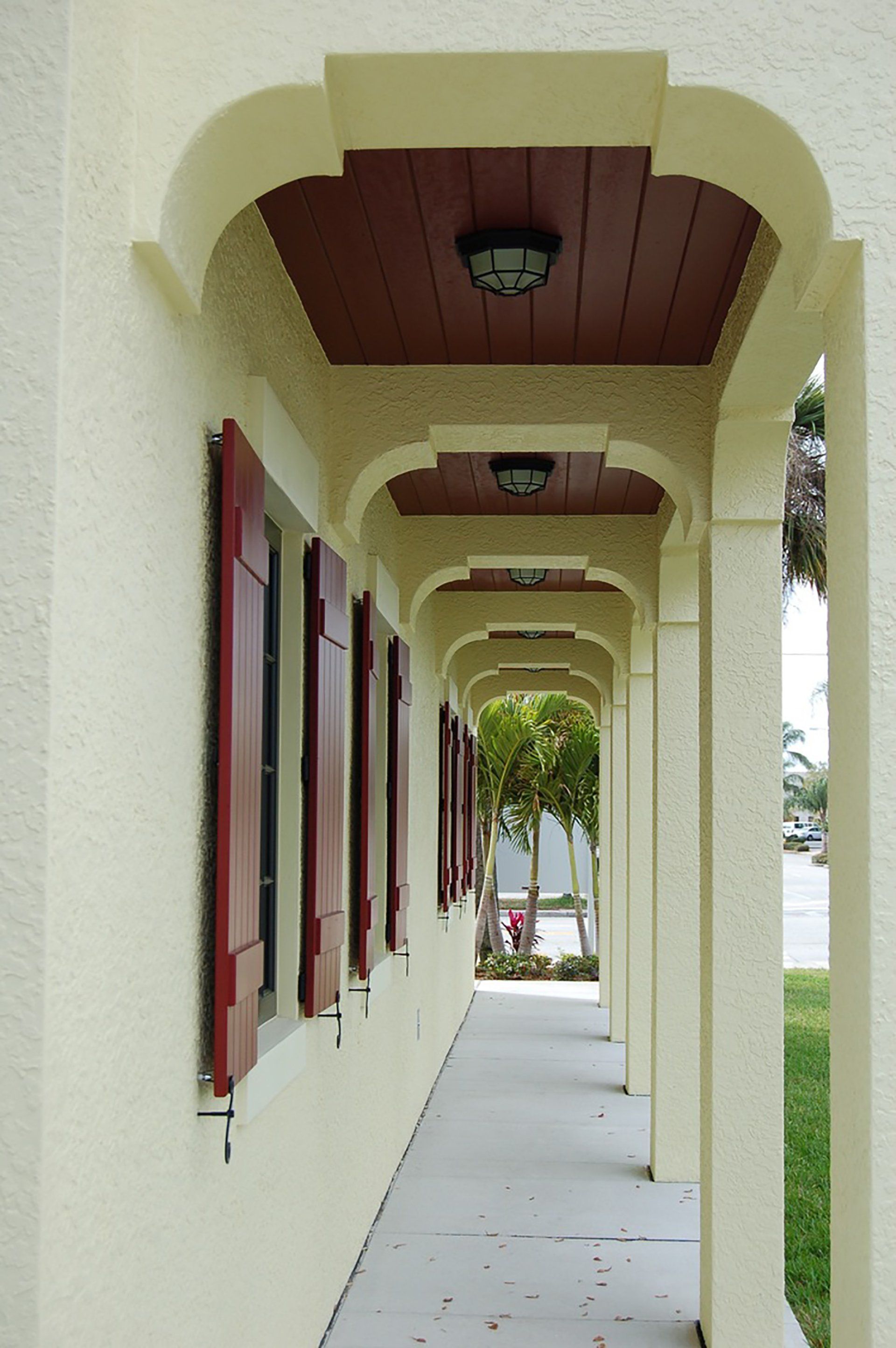 a long hallway with arches and red shutters on the windows