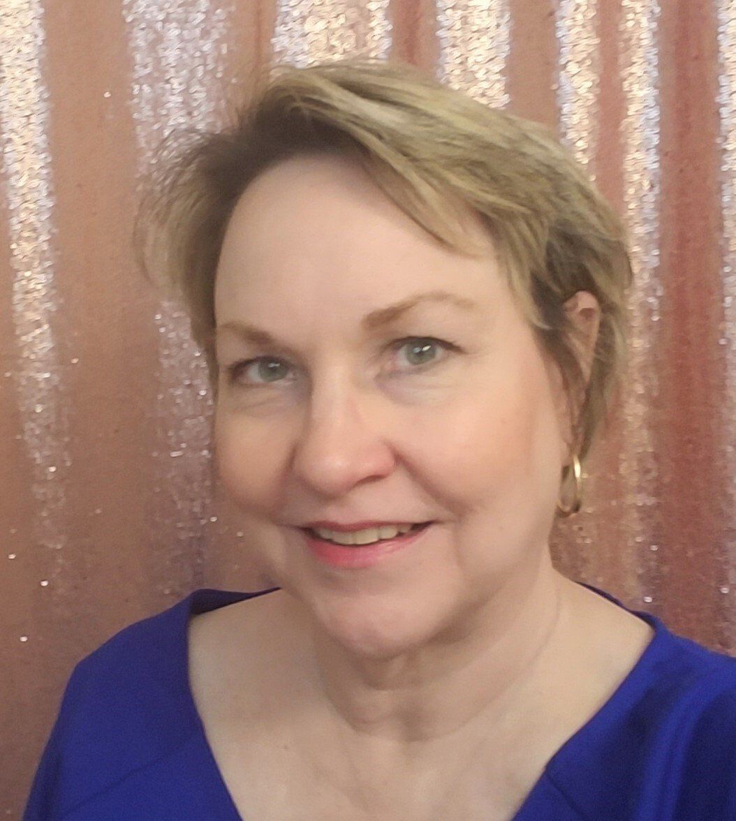 a woman in a blue shirt is smiling in front of a pink curtain .