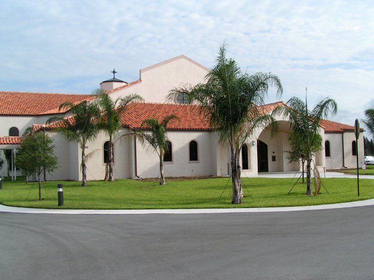 a white building with a red tile roof and palm trees in front of it