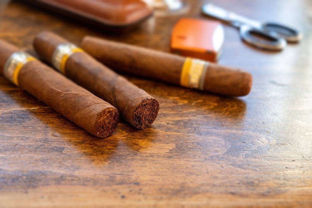 Three cigars are sitting on a wooden table next to a pair of scissors.