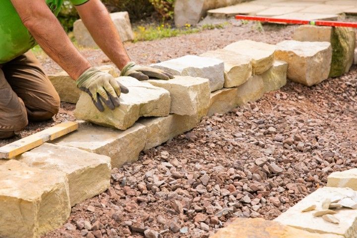 A man is kneeling down to build a stone wall.