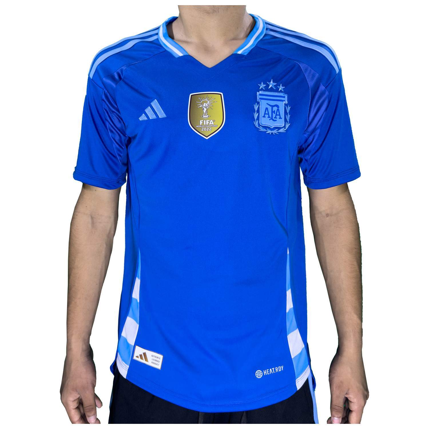 Una persona vistiendo una camiseta de fútbol azul de Argentina con el logo de Adidas y el parche de la Copa Mundial de la FIFA.