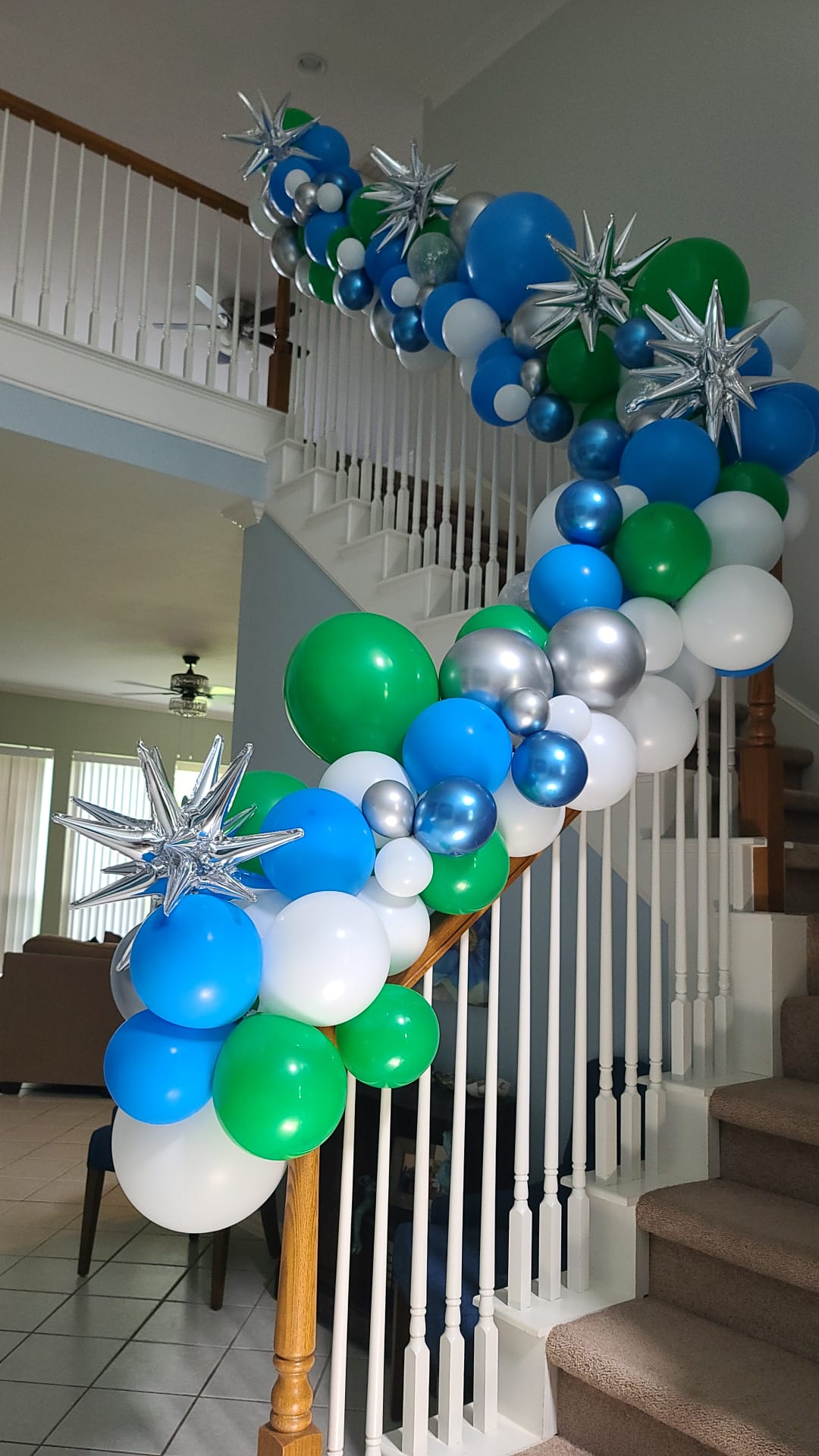 A staircase decorated with blue , green , and white balloons.