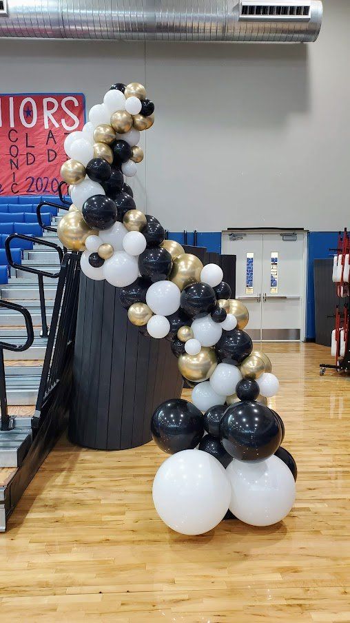 A bunch of balloons are sitting on a wooden floor in a gym.