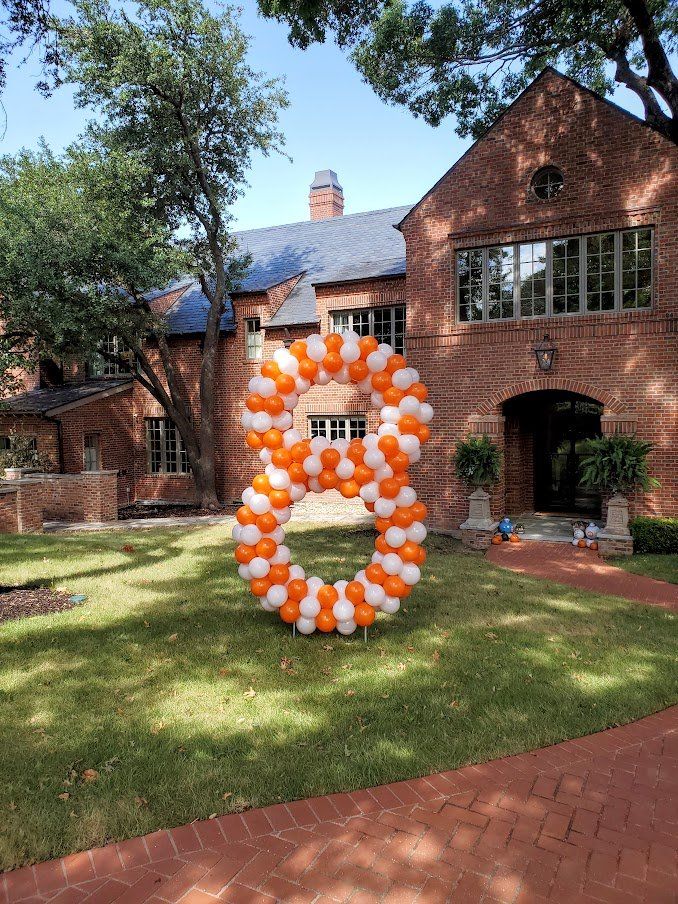 A large number 8 made of orange and white balloons in front of a brick house