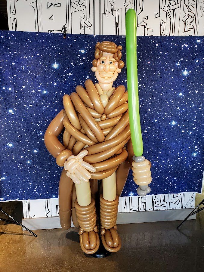 A man made out of balloons is holding a green light saber