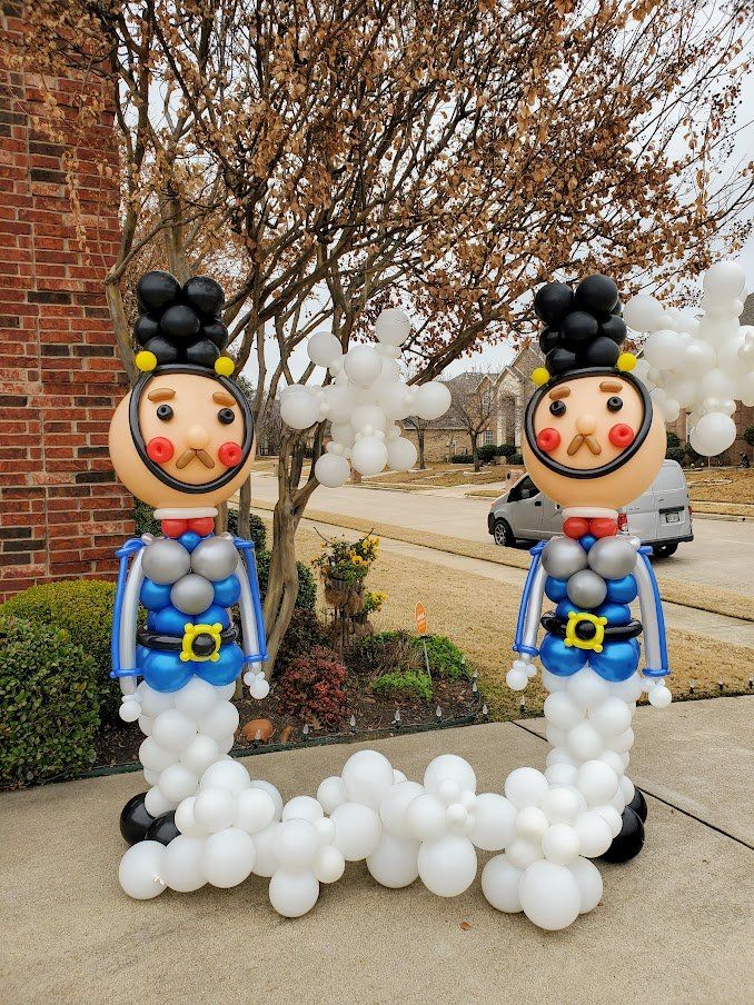 Two nutcrackers made out of balloons are standing next to each other on a sidewalk.