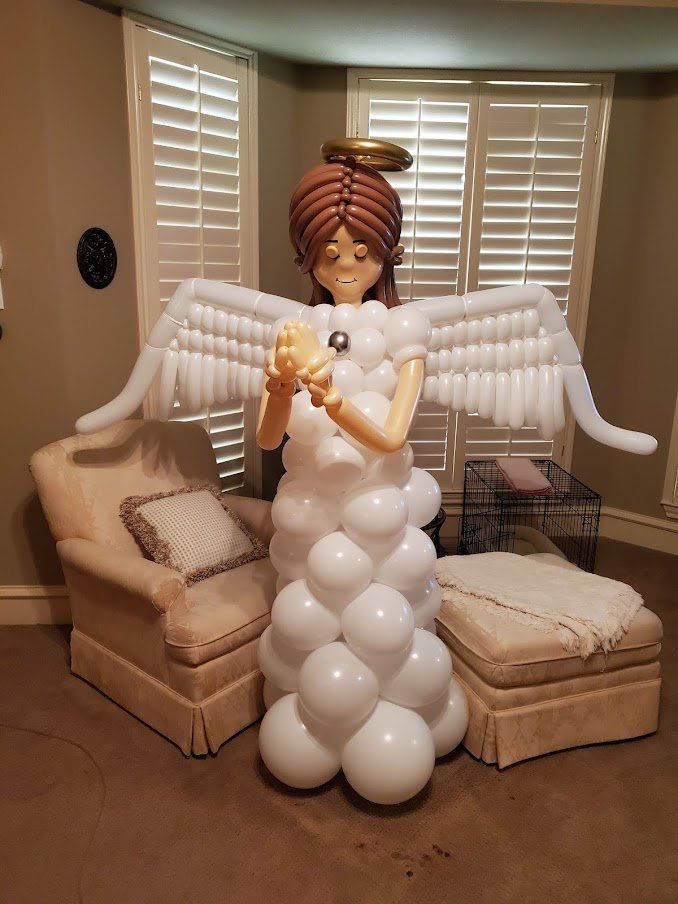 A balloon angel is standing in a living room next to chairs and ottomans.