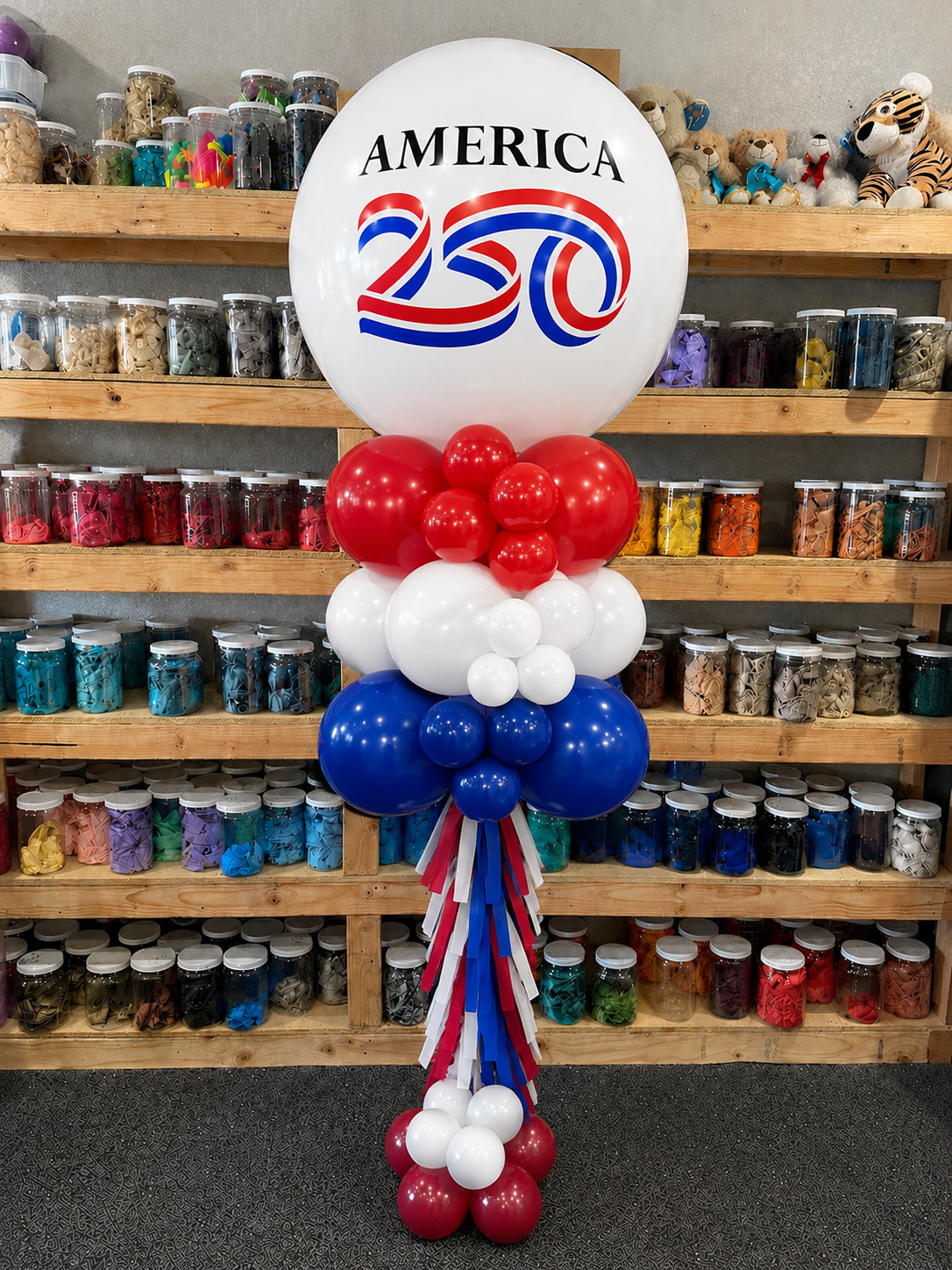 a white jumbo balloon celebrating America's 250th birthday with red, white, and blue matching balloons and tassels.
