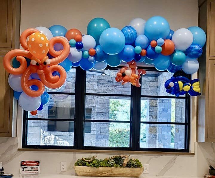 A bunch of balloons are hanging from a window in a kitchen.