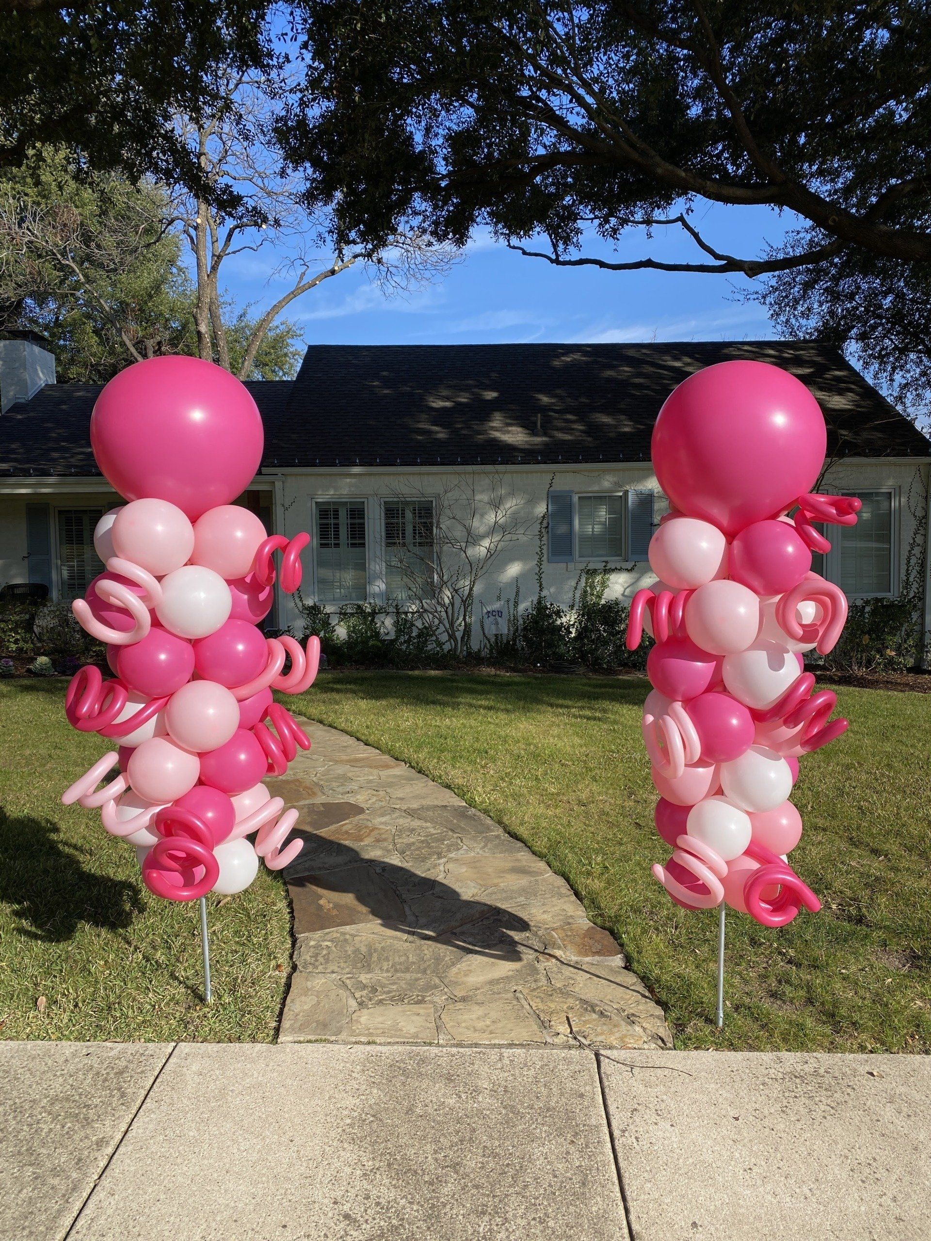 A couple of pink and white balloons sitting in front of a house.
