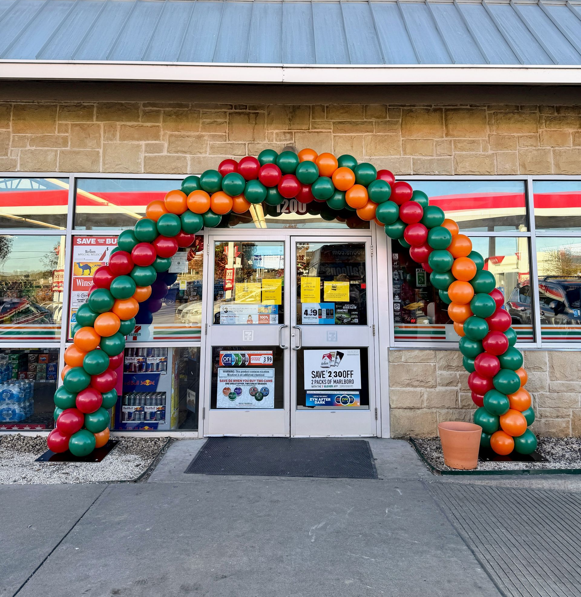 Balloon arch in red, green and orange balloons framing the entrance way of a 7-11 store