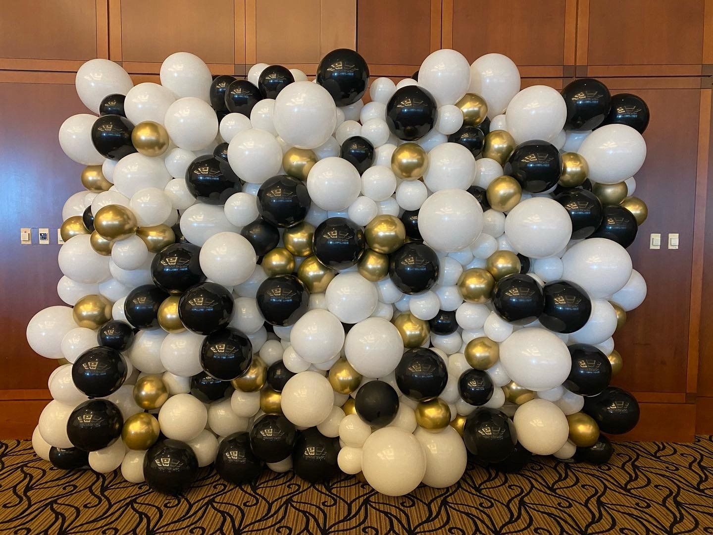 A wall filled with black , white and gold balloons.