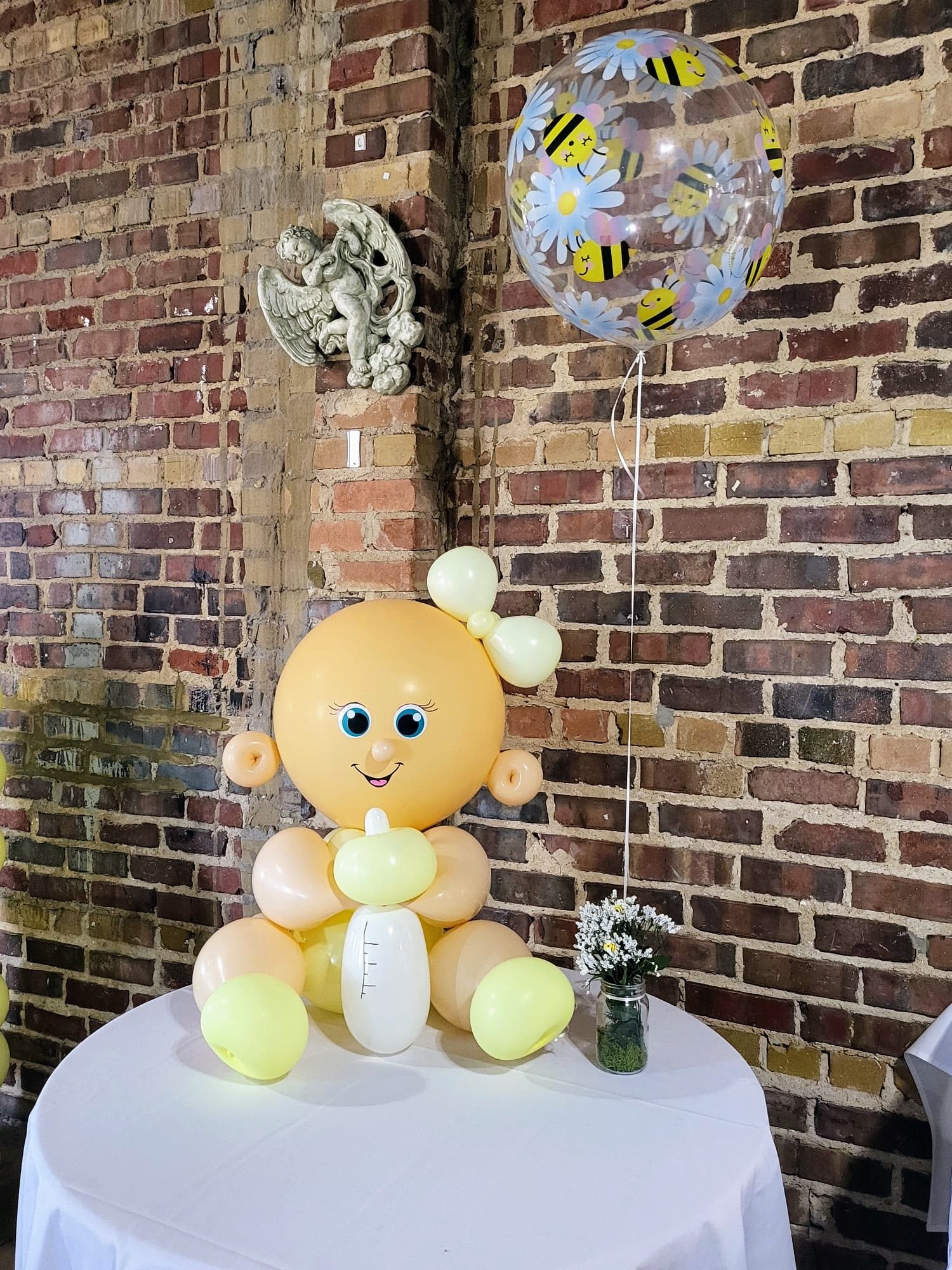 A baby made out of balloons is sitting on a table next to a brick wall.