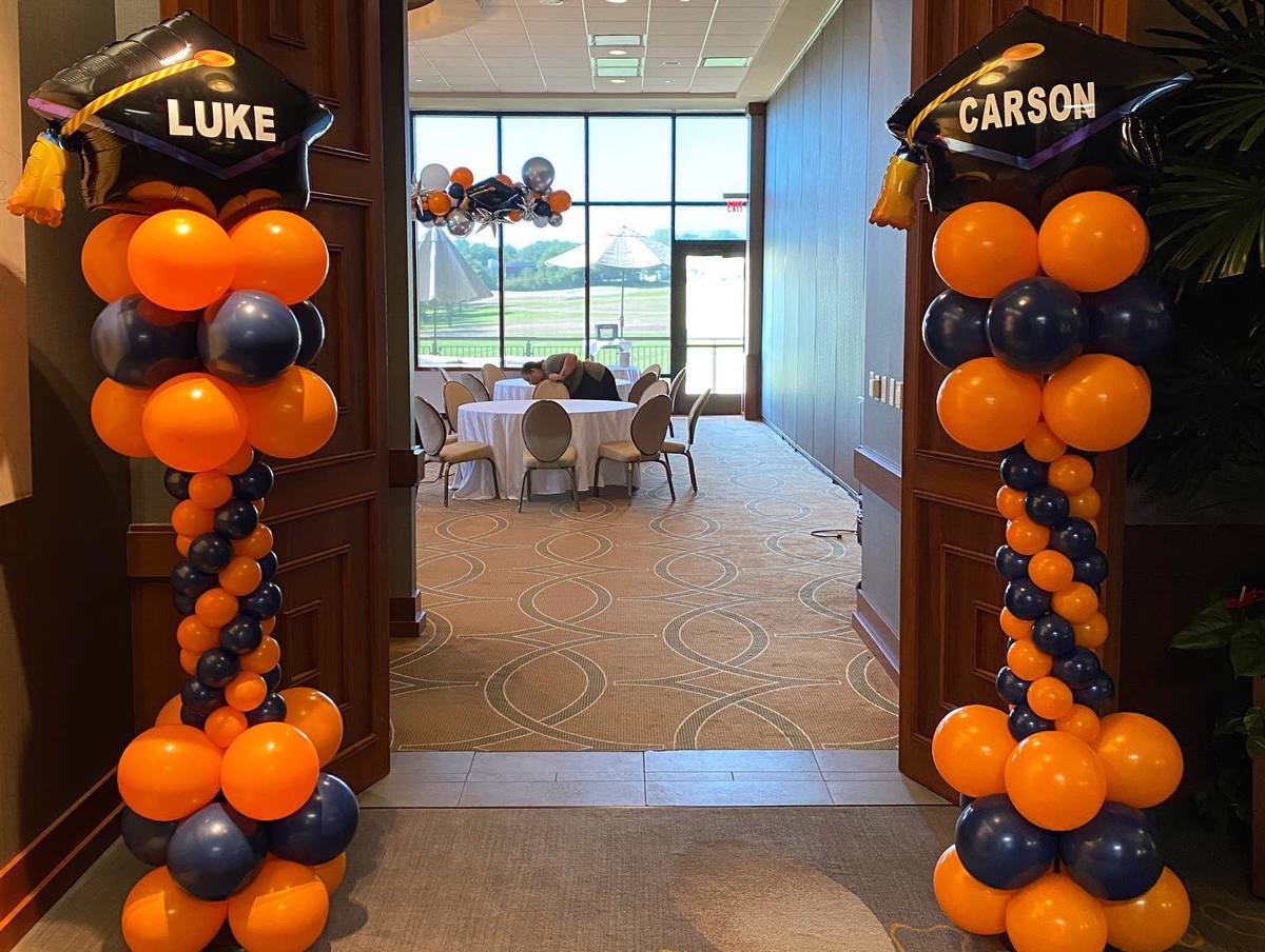 Two columns of orange and blue balloons with graduation caps on them