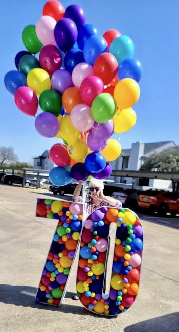 A person is holding a bunch of balloons in the shape of the number 70