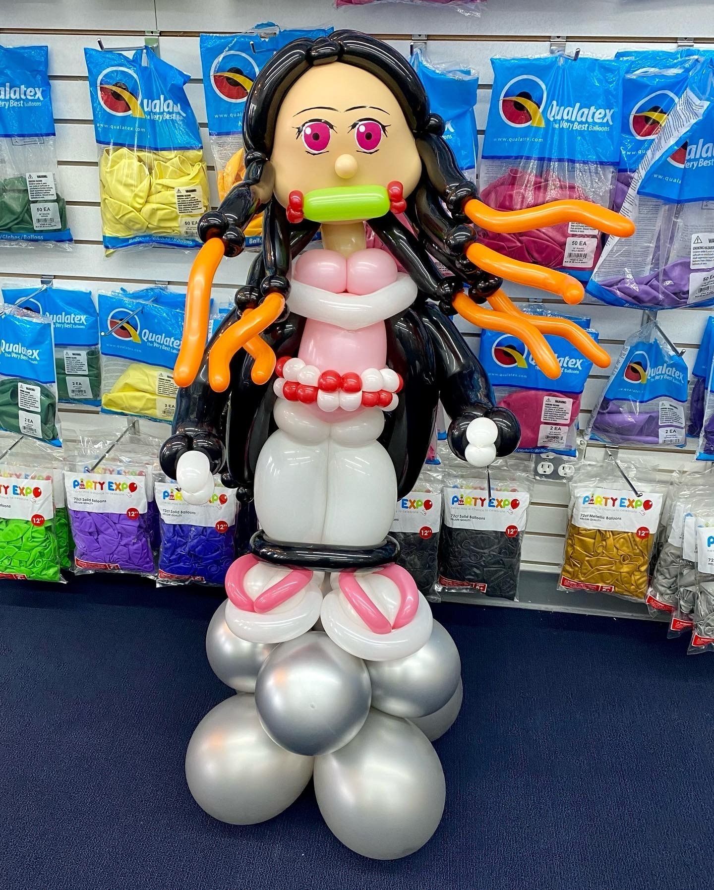 A girl made out of balloons is standing in front of a wall of balloons.