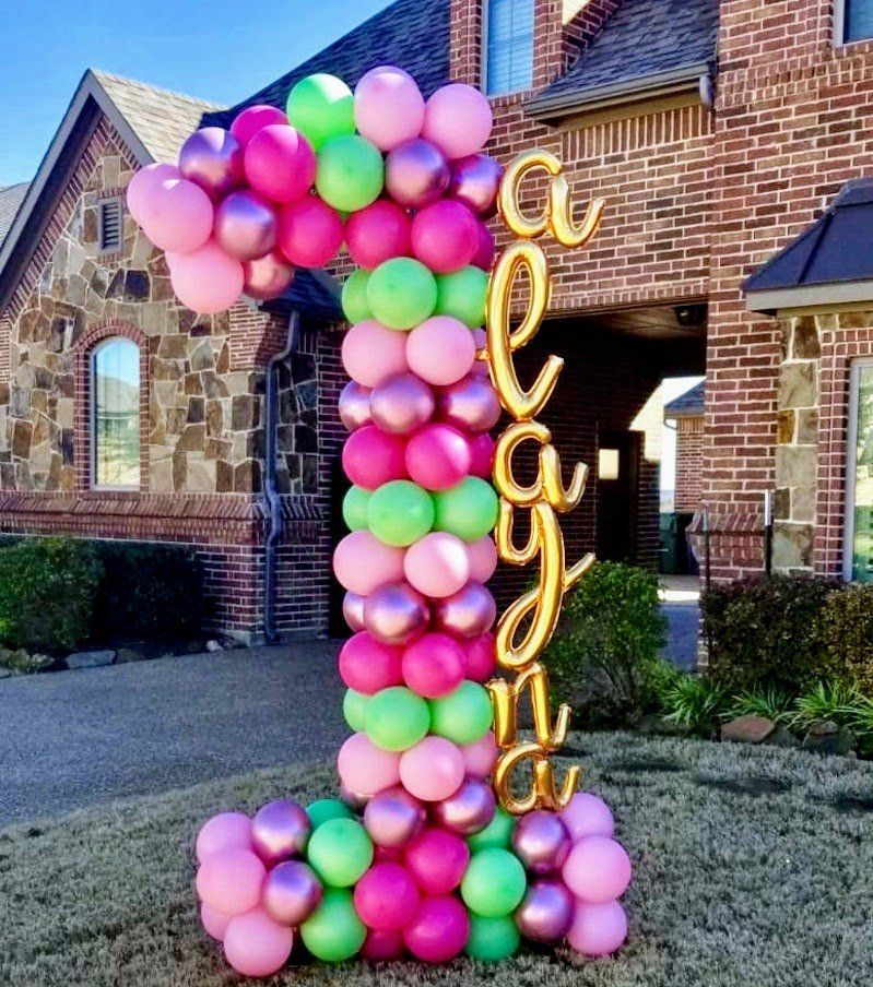 A large number 1 made of pink and green balloons is in front of a brick house.